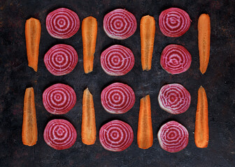 Sliced beetroot and carrot arrange in pattern on dark background. Top view with copy space