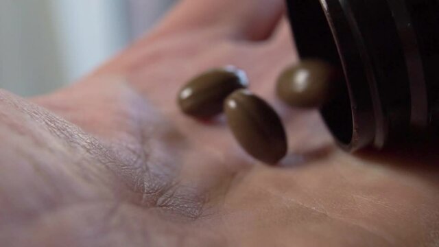 Brown oval medical capsule pills fall into the palm of the hand in slow motion. Macro shot. Prescription treatment concept with natural supplements. Sedative medicine