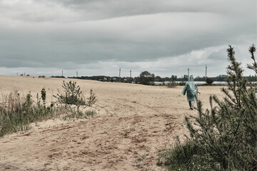 Cloudy sky and sand, in the background a man in a green raincoat. Travel in any weather.