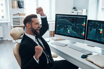 Happy young man in shirt and tie cheering and gesturing while working in the office