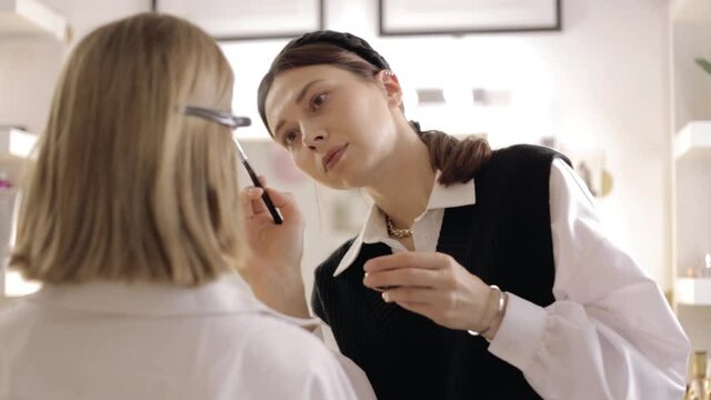 Focused female makeup artist applying eyeshadows on face of unrecognizable model while doing markup in beauty studio 