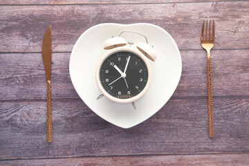 Alarm clock on plate on wooden table, top view.
