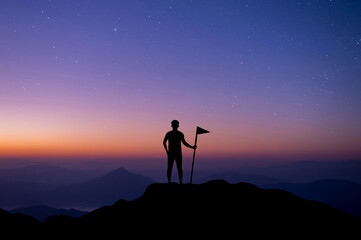 Silhouette of young people standing looking at the sky and the stars at night and hand holding a flag on the top of the mountain alone. He enjoyed the journey and felt successful.