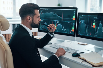 Concentrated young man in shirt and tie analyzing data on the stock market while working in the...