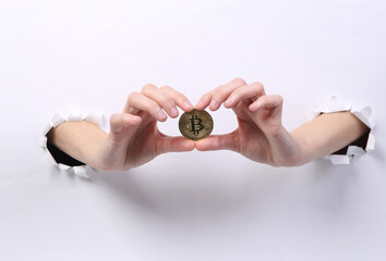 Female hands holding bitcoin through torn hole white paper. Concept art
