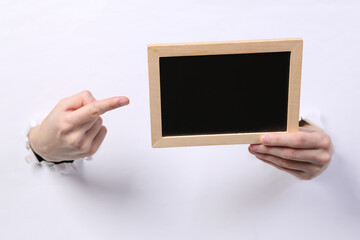 Female hands holding blank chalk board through torn hole white paper. Copy space