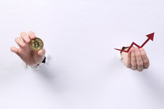 Female hands holding bitcoin and growth arrow through torn hole white paper. Concept art