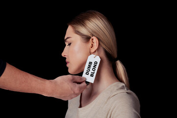 Hand of man touch face of upset young woman with label on ear is dumb blonde