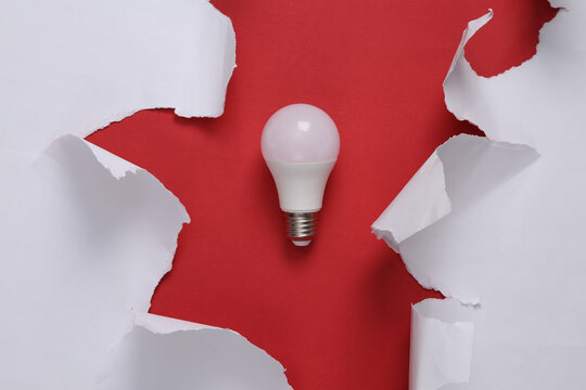 Led light bulb and white torn paper sheets on red background. Top view
