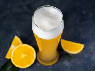 Wheat fruit beer in a glass, orange slices, dark background. Summer refreshing craft beer