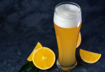 Wheat fruit beer in a glass, orange slices, dark background. Summer refreshing craft beer