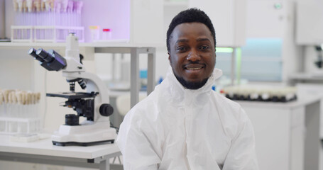 Afro-american male scientist in overalll smiling at camera in lab