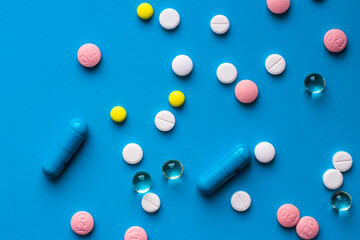 Many multicolored pills and capsules on a blue background