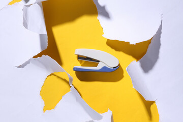 Stapler on yellow background with white torn paper. Minimalism. Trend shadow. Top view