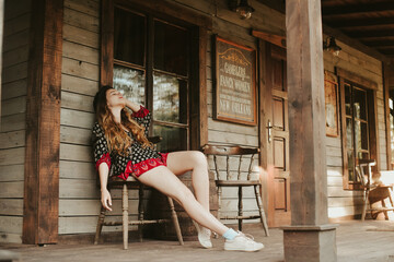 A woman is resting on a terrace near a western house, a weekend in an interesting hotel. Travel alone. Long-legged woman resting after work on the farm.