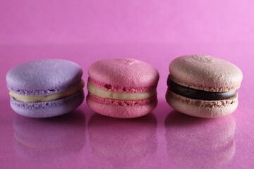 Obraz na płótnie Canvas Three macaroons lilac brown chocolate lavender pink lie in a row on a pink fuchsia-colored background with reflection and a place for text and copyspace