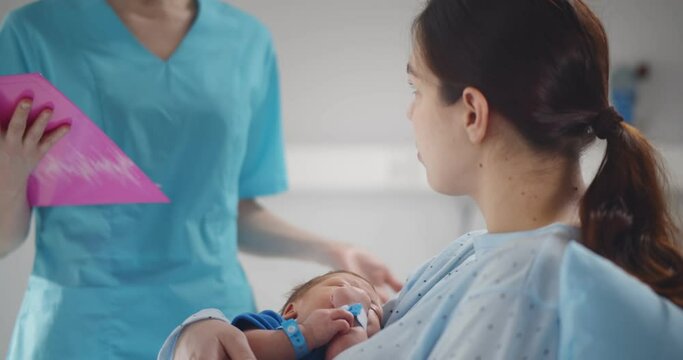 Happy mother holding newborn baby talking to doctor in hospital