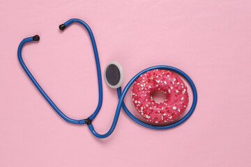 Health care. Stethoscope and high-calorie donut on a pink background. Junk food