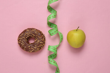 Slimming concept. Healthy or junk food. Donut and apple with measuring ruler on pink background