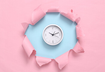 Clock through torn hole on blue-pink pastel background. Business concept. Pastel color trend....