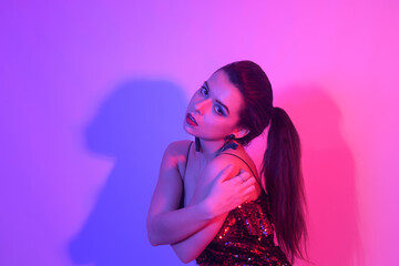 A girl in neon is dancing against a red-blue background. Hipster girl with fashionable haircut and glasses dancing, posing. Model in a fur coat at the club.