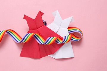 Lgbt community. Origami dresses and rainbow ribbon on pink background