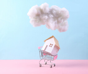 Shopping trlley with house, floating fluffy cloud on blue pink pastel background. Concept art. Minimalistic idea