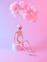 Modern composition of skeleton and floating fluffy cloud in blue pink neon gradient light. Creative idea. Halloween Concept. Minimalism. Surrealism