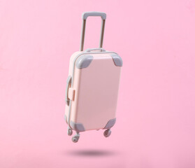 Mini travel luggage soaring on a pink background. Minimalism travel concept