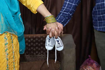 Close up picture of happy couple of pregnant mother with father holding hands small shoes. Indian couple hands holding baby boys shoes