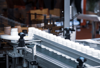 White plastic bottle on capsule filling machine conveyor belt in production line. Pharmaceutical...