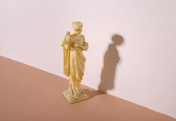 Creative vintage still life. Antique goddess sculpture on beige brown  background. Minimalism. Trendy shadow.