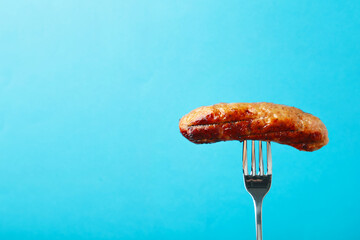 Grilled sausage on a fork on blue background with copy space