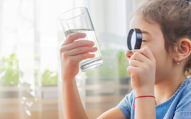 The child examines the water with a magnifying glass in a glass. Selective focus.