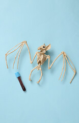 Bat skeleton and test tube with blood on blue background