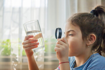 The child examines the water with a magnifying glass in a glass. Selective focus.
