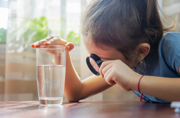 The child examines the water with a magnifying glass in a glass. Selective focus.