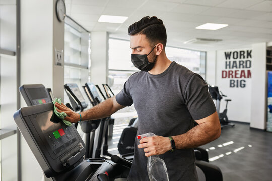 Fit Muscular Gym Guy Disinfecting Treadmill After Workout Wearing Face Mask