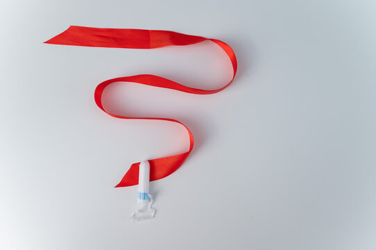 Tampon and red satin ribbon on a white background. Means of intimate hygiene of a woman during mentruation