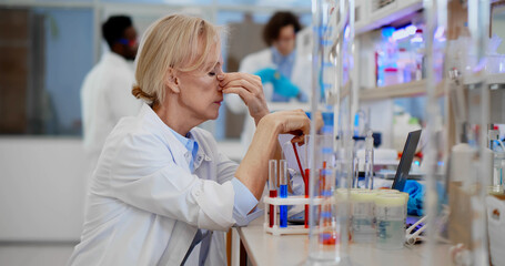 Exhausted research scientist sitting at desk in chemical laboratory.