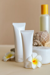 Fototapeta na wymiar Natural beauty cosmetic tube mockup product for skincare with sea shell tropical plumeria flowers on stone pedestal beige background. Natural body care sun protect cream cosmetic tube