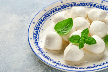 Mozzarella cheese with basil in white ceramic plate, tomato cherry olive oil and spice grinder, condiments, pepper tomato cherry on slate stone background. Mock up. Ingredients for Caprese salad.