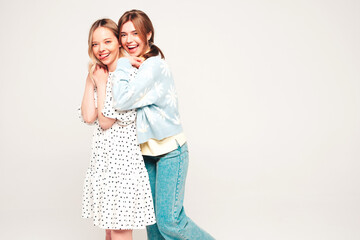 Two young beautiful blond smiling hipster female in trendy summer clothes. Sexy carefree women posing on grey background in studio. Trendy and positive models having fun