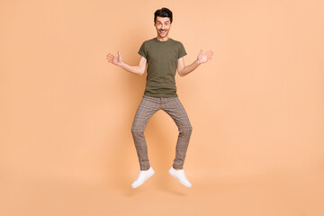 Fototapeta na wymiar Full length body size photo of jumping funny man smiling wearing casual clothes isolated on pastel beige color background