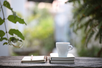 White coffee cup and notebooks with pencil on wooden table at outdoor