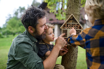 Small children with father holding bug and insect hotel in garden, sustainable lifestyle.