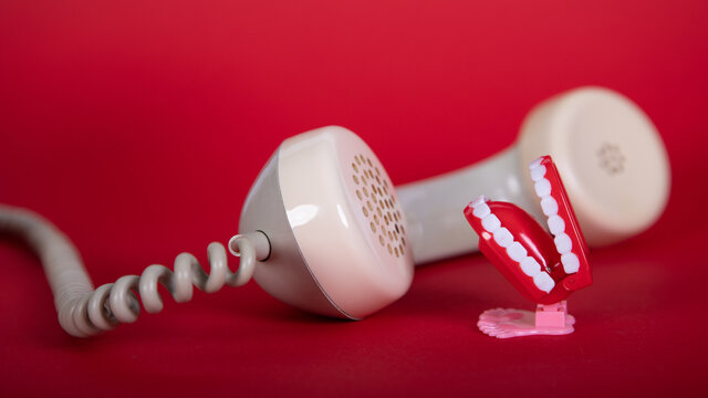 alter Telefonh&ouml;rer und ein Spielzeugmund mit Z&auml;hnen, als Symbol f&uuml;r das Sprechen am Telefon, roter Hintergrund