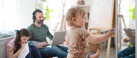 Father working with small daughters in bedroom, home office concept.
