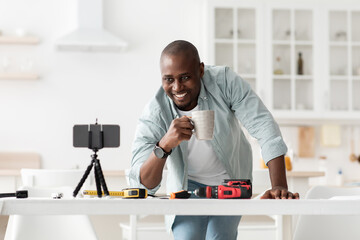 Shooting video instructions for self assembly of furniture. Happy black man with cup of coffee looking at smartphone
