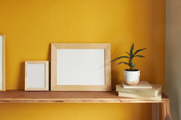 Wooden pictures frame mockup. Flowerpot on a pile of books on an old wooden shelf. Composition on a yellow wall background